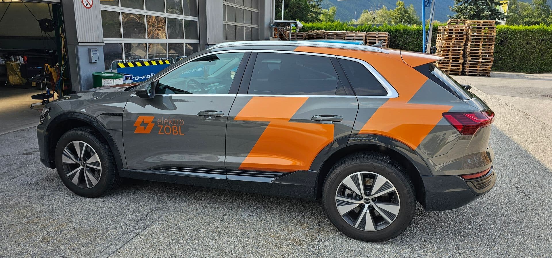 Grauer Audi e-tron mit oranger Blitzgrafik über der Flanke und Logo eines Elektrobetriebs