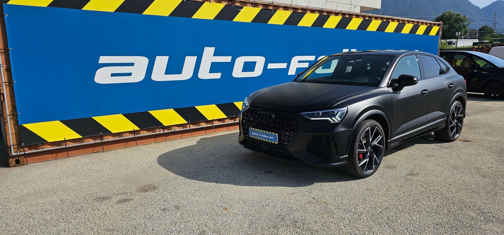 Mattschwarz folierter Audi RS Q3 Sportback vor der blau-gelben Firmenplane von auto-folien.at