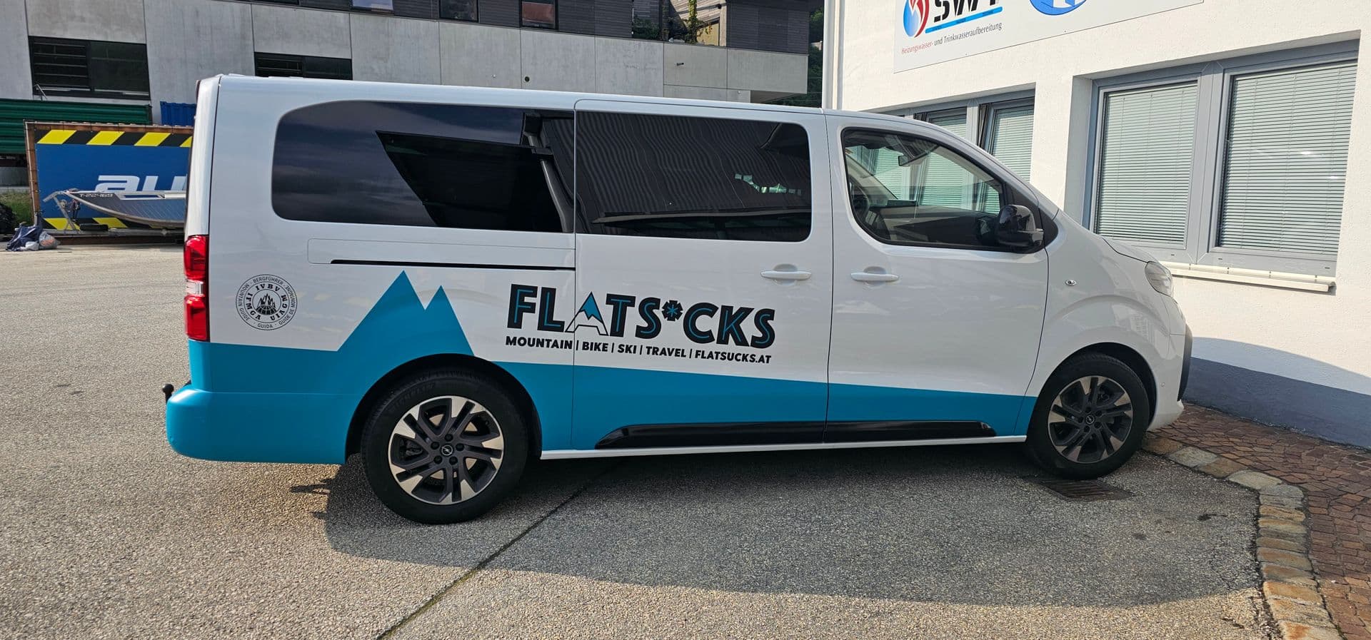 Weiß-türkiser Kleinbus mit Berggrafik und Markenschriftzug, die hinteren Scheiben sind getönt