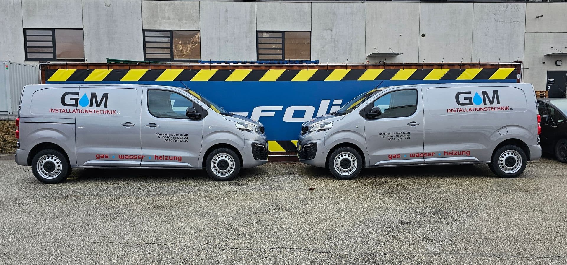 Zwei silberne Peugeot Expert eines Installationsbetriebs nebeneinander vor der Firmenplane von auto-folien.at