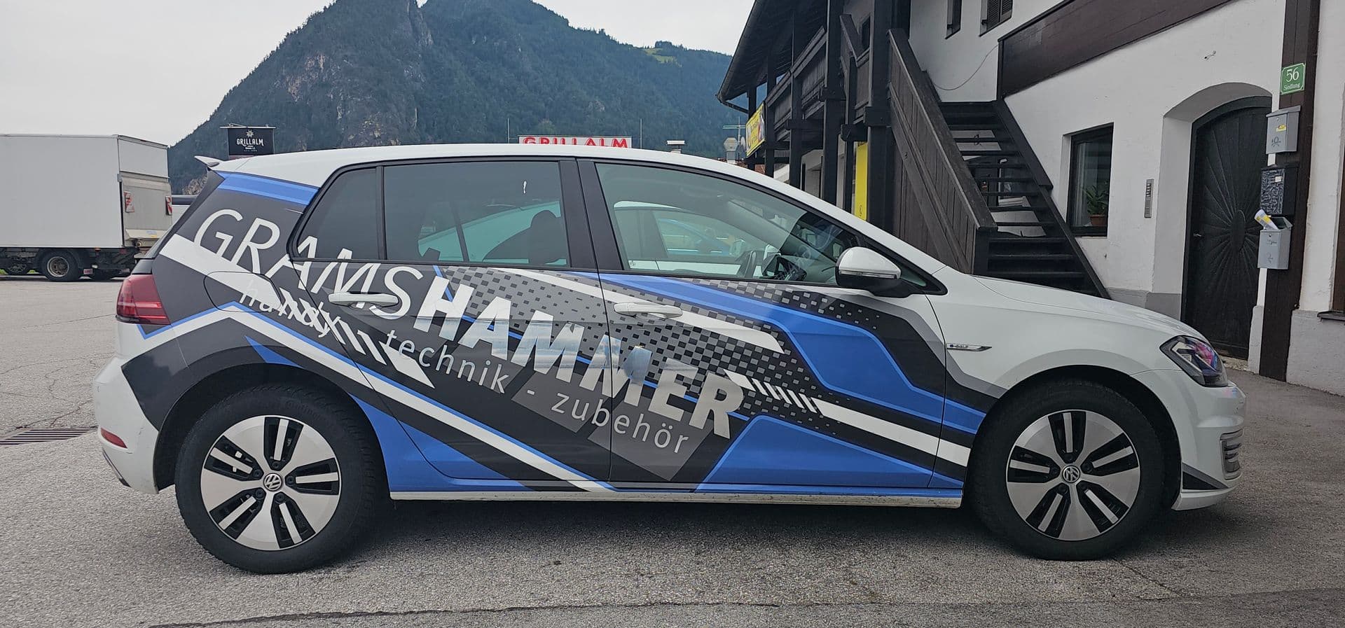 Weißer VW e-Golf mit blau-grauer Splittergrafik und Beschriftung eines Handytechnik-Betriebs
