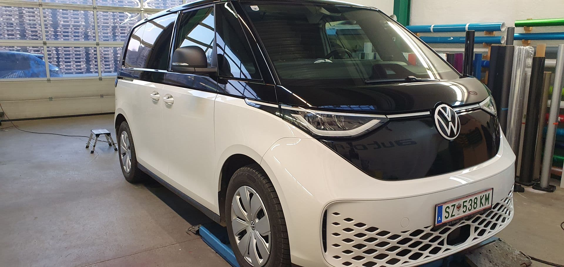 VW ID. Buzz in zweifarbiger Folierung auf der Hebebühne, an der Wand das Folienlager der Werkstatt