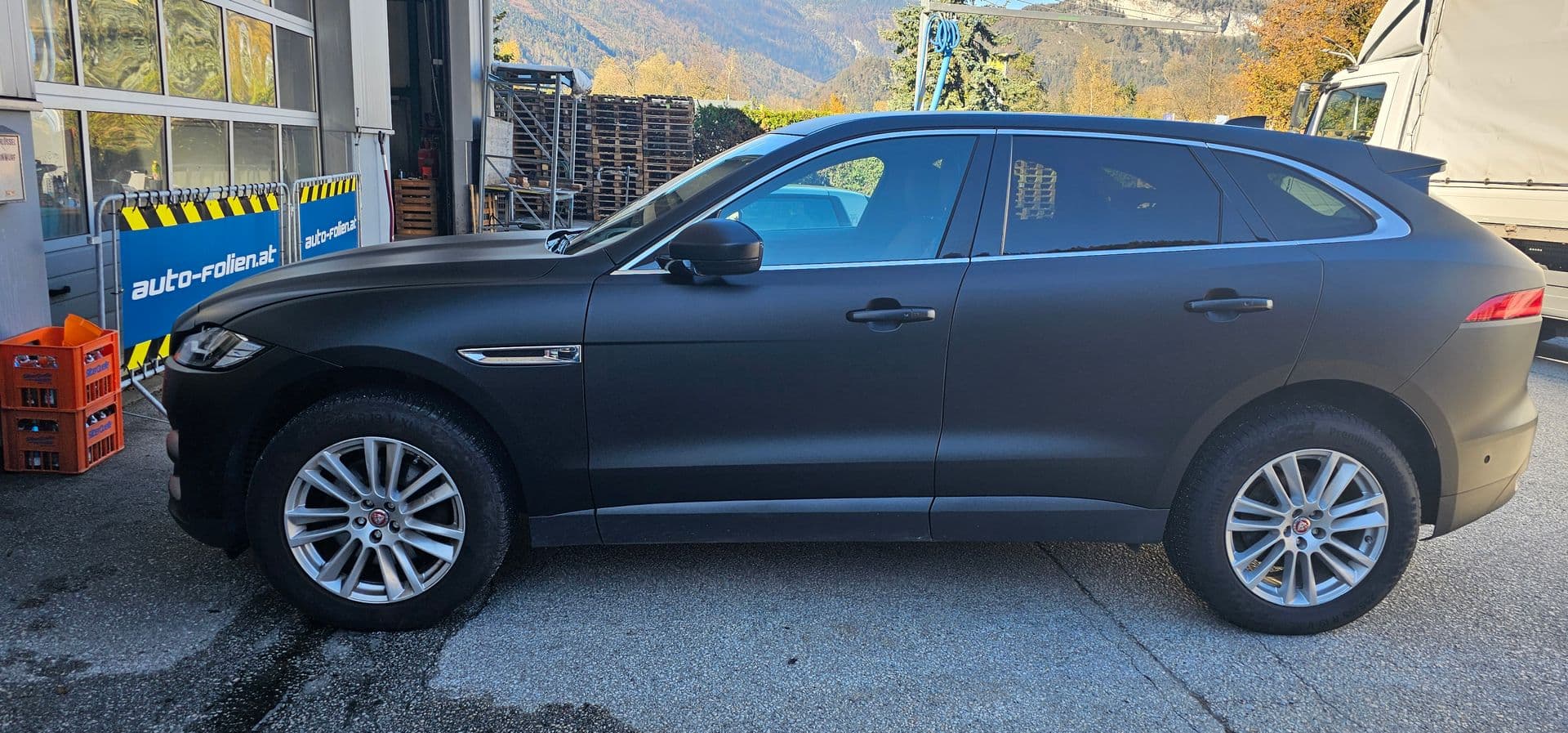 Mattschwarz folierter Jaguar F-Pace in der Seitenansicht vor der Werkstatthalle von auto-folien.at