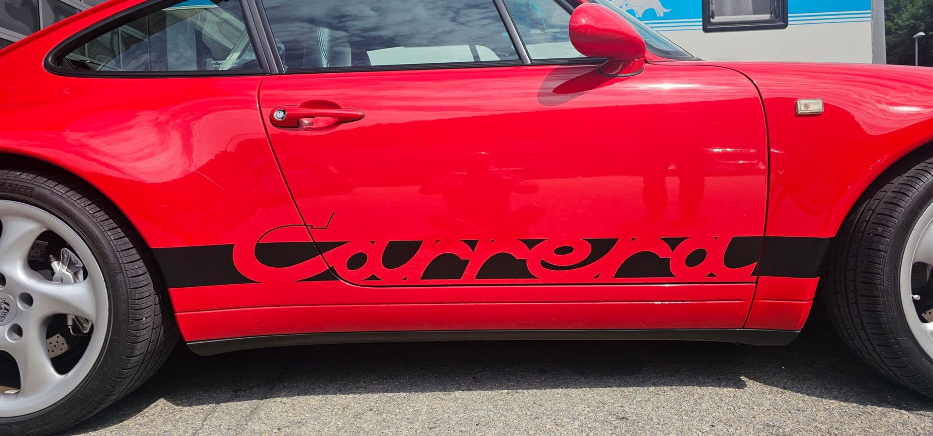 Detailaufnahme der Flanke eines roten Porsche 911 mit schwarzem Carrera-Schriftzug als Seitenbeschriftung