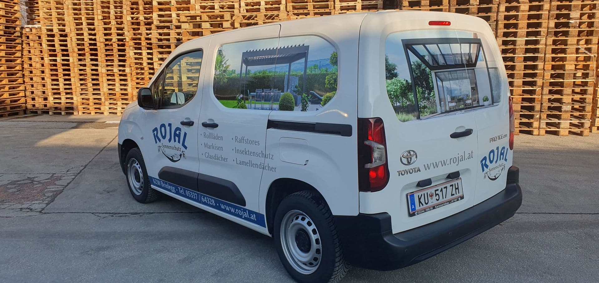 Weißer Toyota Proace City mit blauer Beschriftung und gedrucktem Terrassenmotiv im Seitenfenster