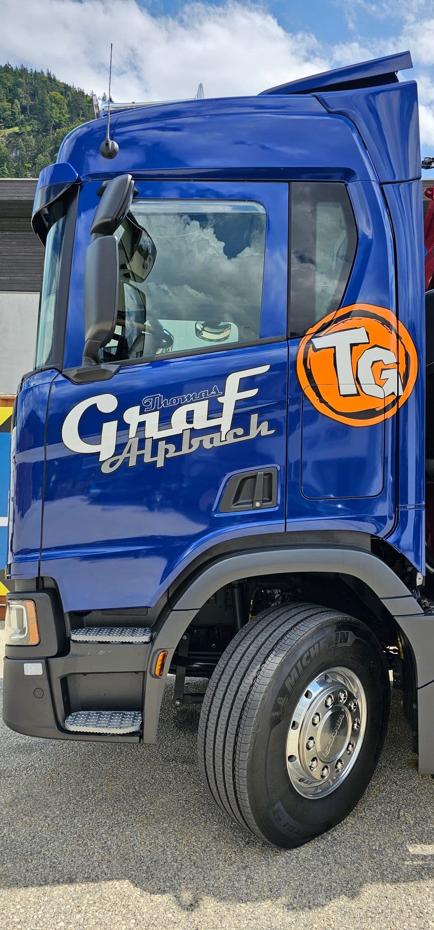 Blaues Scania-Fahrerhaus mit verchromtem Schriftzug und rundem Logo eines Alpbacher Transportunternehmens