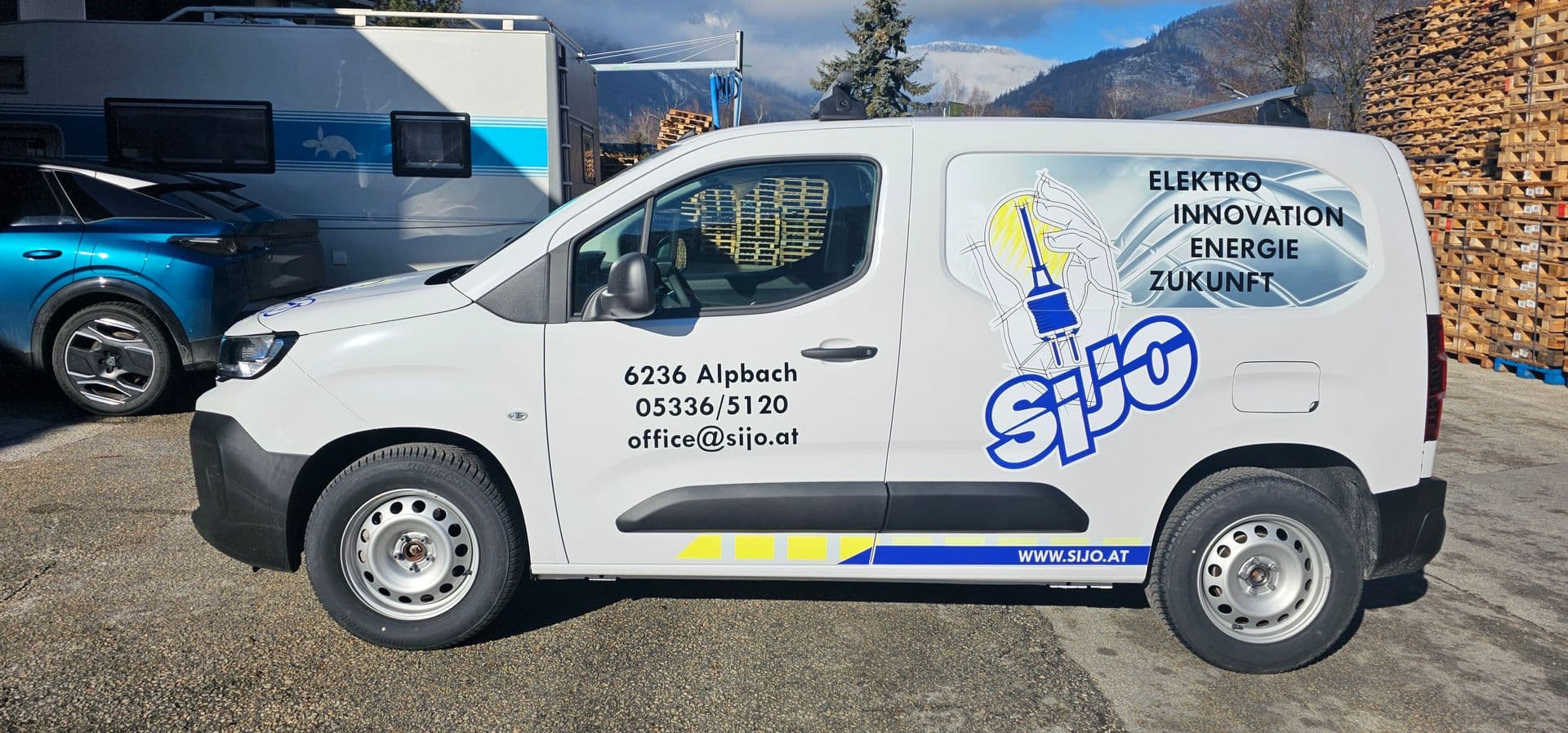 Weißer Peugeot Partner mit blau-gelber Beschriftung eines Alpbacher Elektrobetriebs vor verschneiter Bergkulisse
