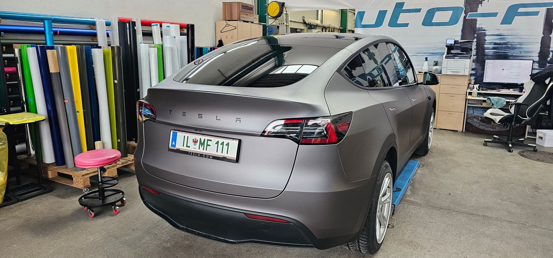 Tesla Model Y in mattem Grau in der Werkstatt, dahinter ein Regal mit aufgerollten Folien
