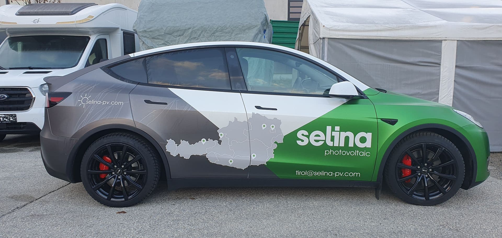 Tesla Model Y mit grün-grauer Beschriftung eines Photovoltaikbetriebs in der Seitenansicht