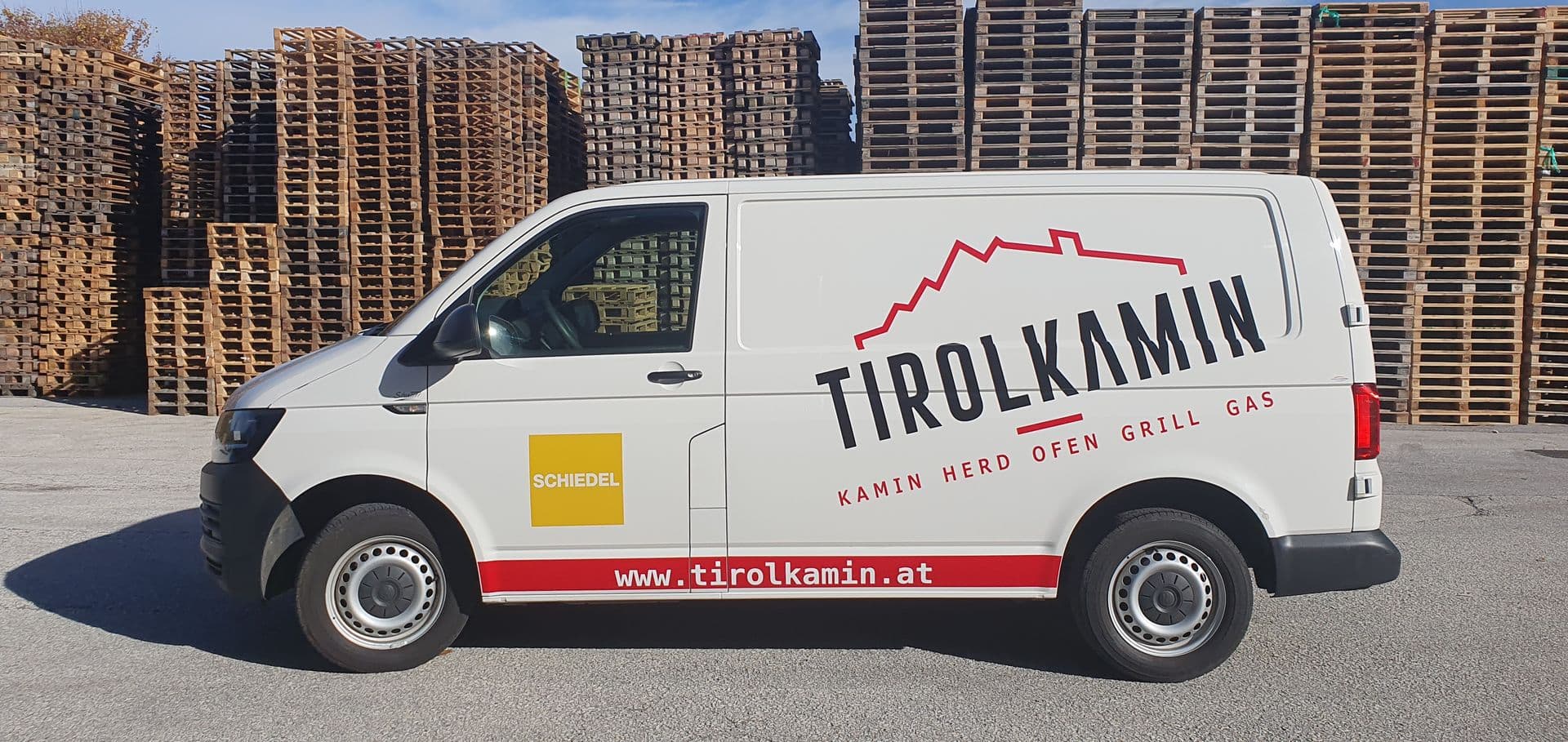 Weißer VW Transporter mit Beschriftung eines Kaminbaubetriebs vor Palettenstapeln