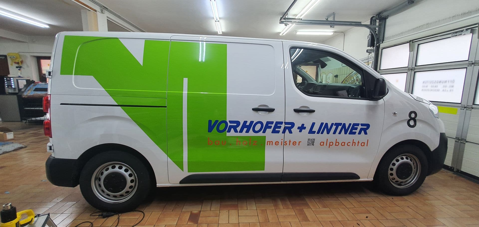 Weißer Peugeot Expert mit grünem Pfeilmotiv und Beschriftung eines Zimmereibetriebs in der Werkstatt