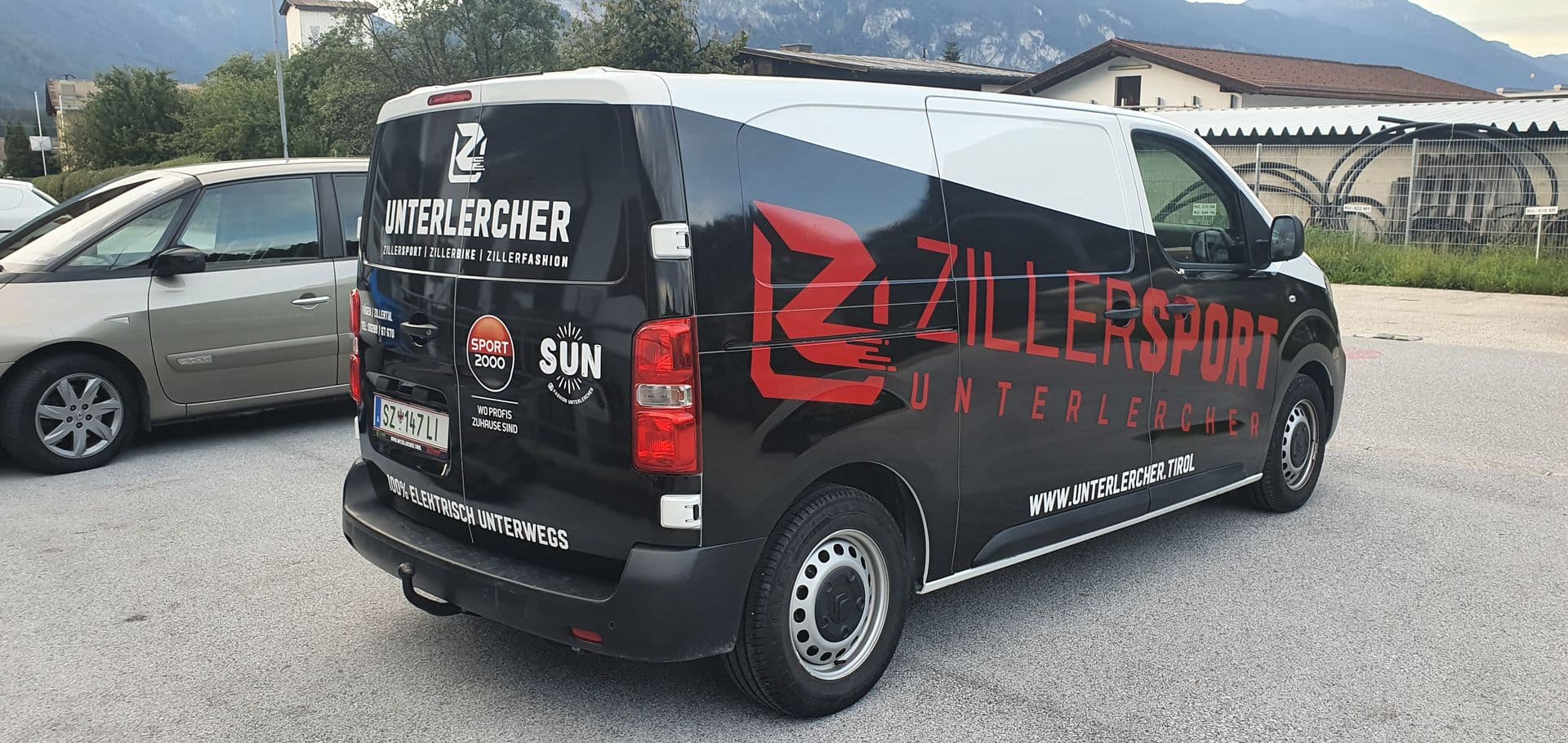 Schwarz-weißer Peugeot Expert eines Sportgeschäfts in der Heckansicht vor Bergkulisse